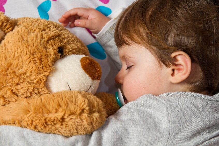 A young child sleeps with a teddy.