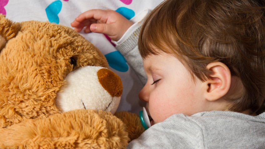 Young boy sleeping with a giant orange teddy bear.