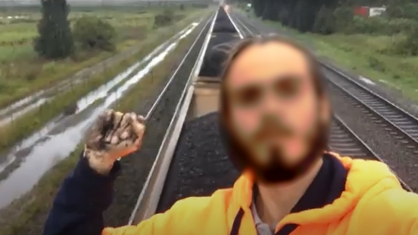 Man with dark haird and beard wearing a yellow hooded jumper, hand in fist on top of a coal train