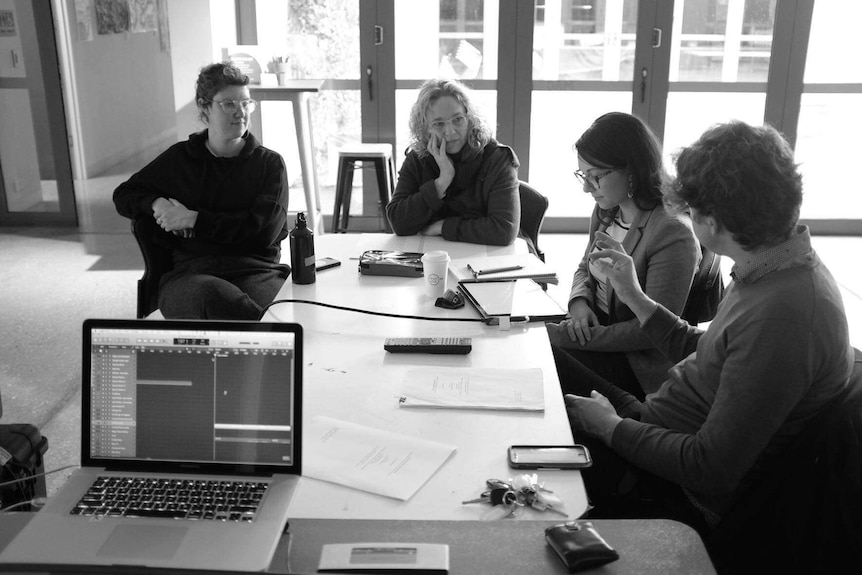 Four women sitting around a table with paper and pens and a laptop in the foreground