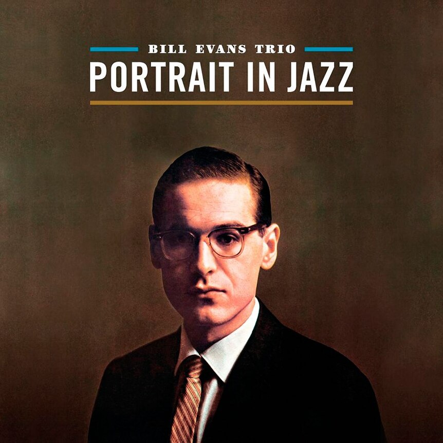 A colour photo of Bill Evans in a suit and glasses looking into the camera