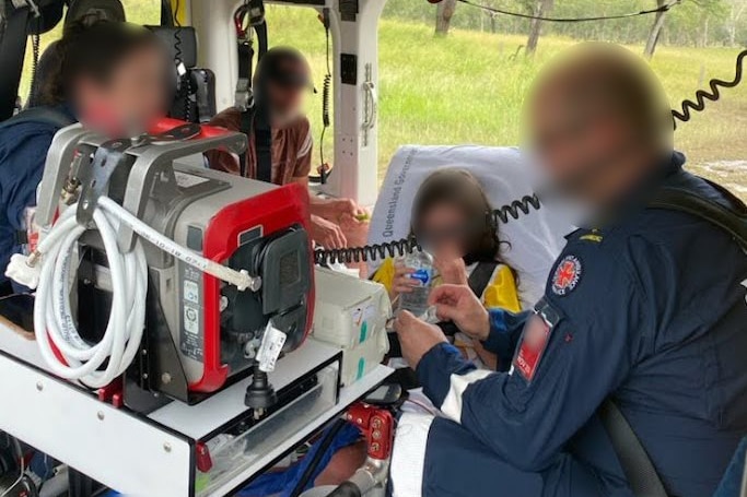 Medical professionals crowd around a young girl in the back of a helicopter. All faces are blurred. 