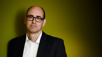 A man in a suit standing against a wall.