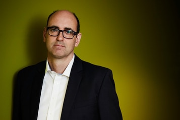 A man in a suit standing against a wall.