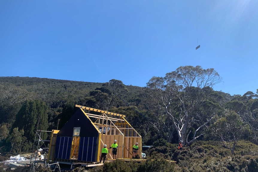 A team of builders working in high vis in a remote bush setting with a helicopter flying in a part overhead