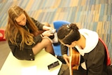 Teenage boy and girl sitting on the carpet looking at phones in classroom.