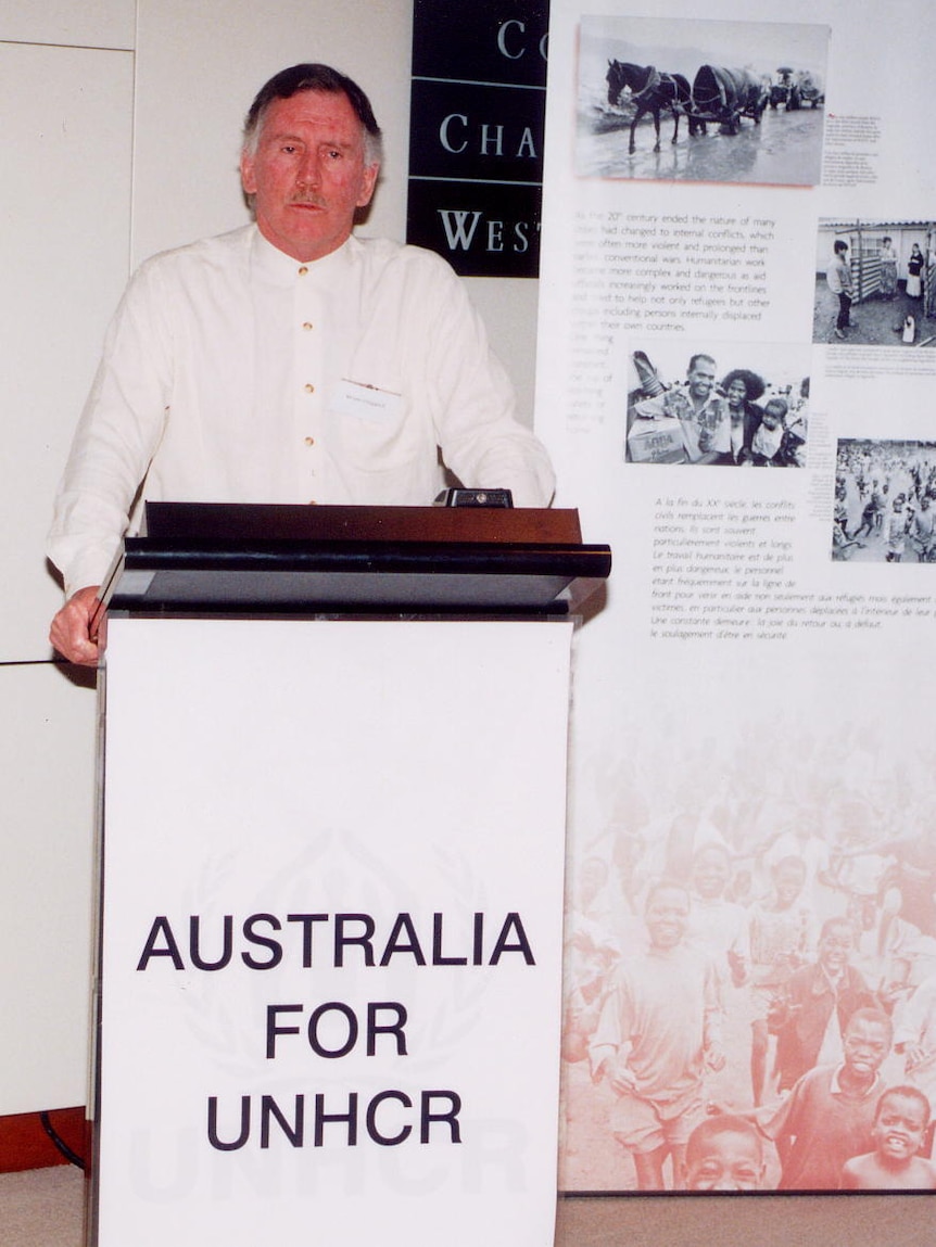 Ian Chappell stands at a lecturn which says Australia for UNHCR.