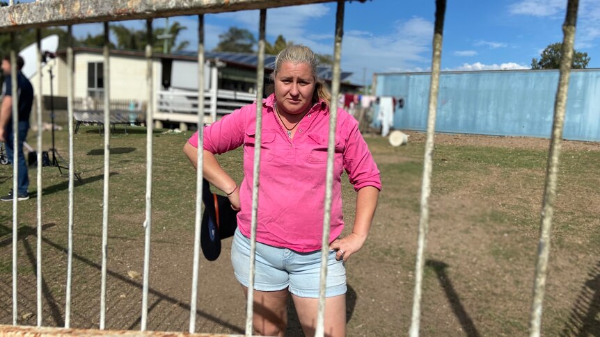 A woman in a pink shirt standing behind a metal fence. 