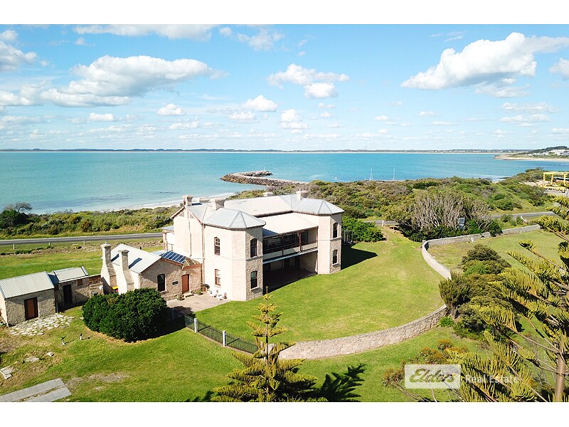 A large stone building on well-kept lawns, a bright blue ocean behind it.