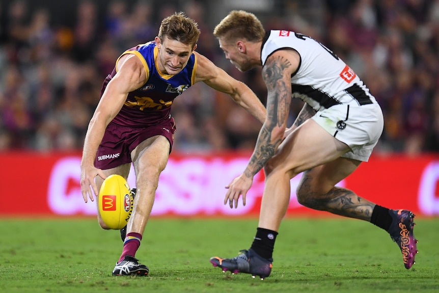 Harris Andrews runs towards a yellow AFL ball with his right arm reaching forward to it