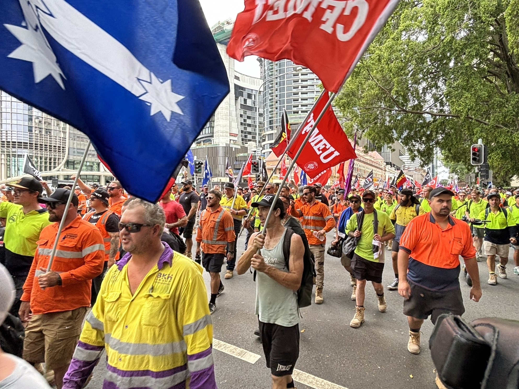 An image of construction workers in high vis workwear marching with flags in Brisbane outside parliament