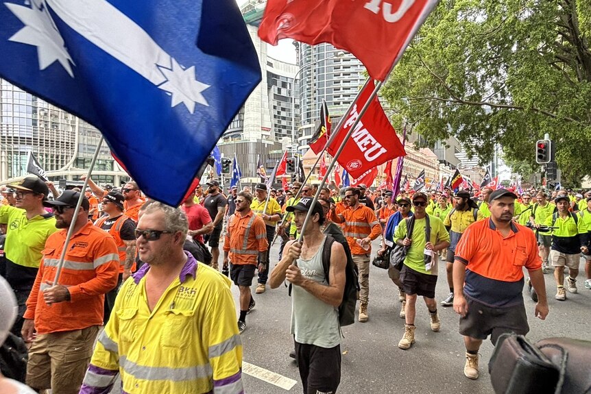 An image of construction workers in high vis workwear marching with flags in Brisbane outside parliament
