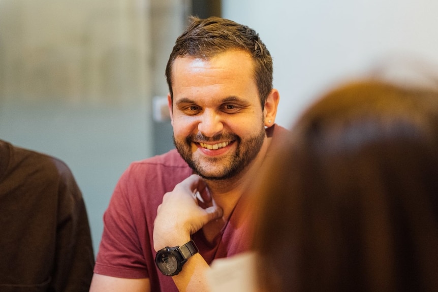 a man in a tshirt smiles as he talks to a woman