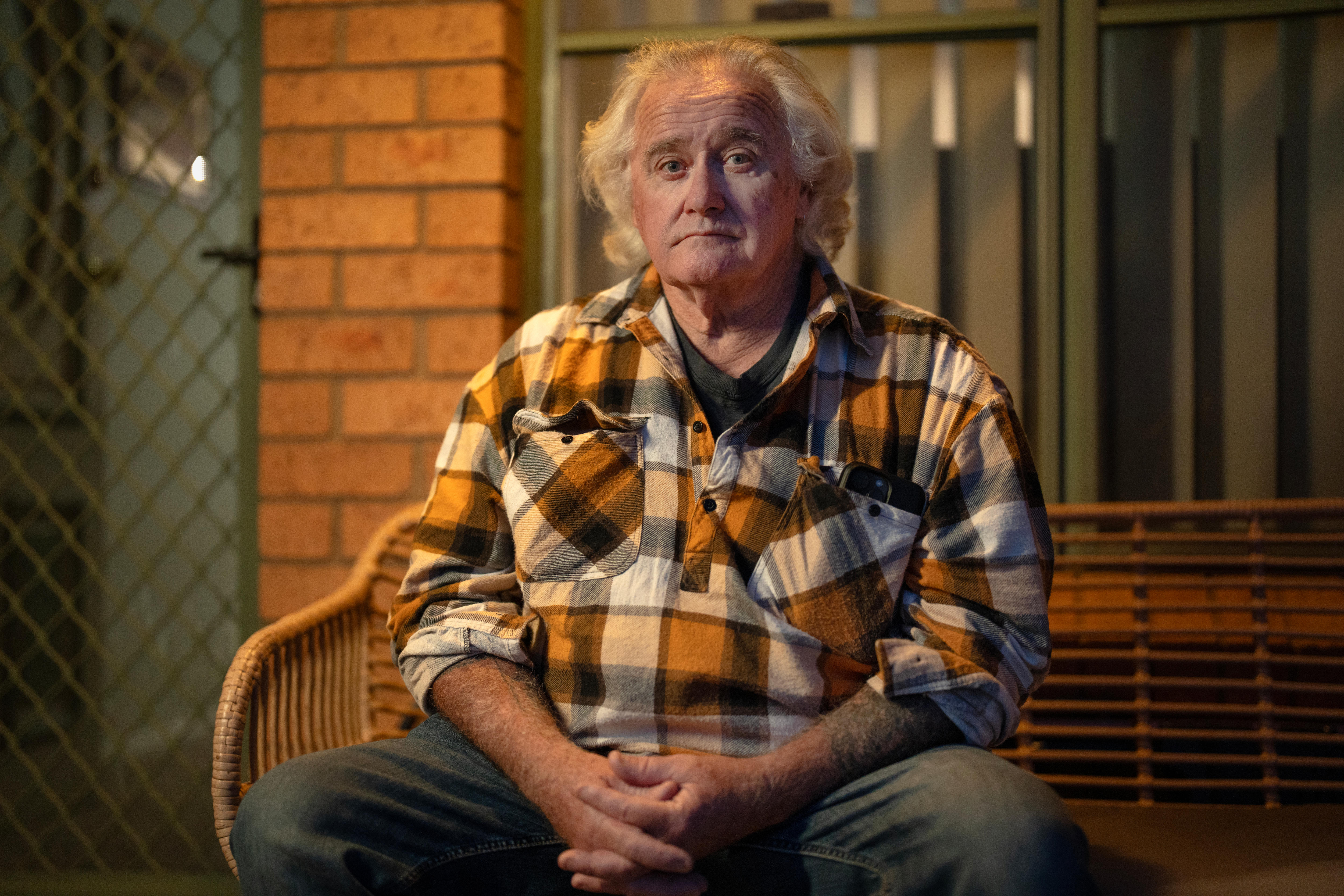 Man sitting on seat on verandah, staring at camera.