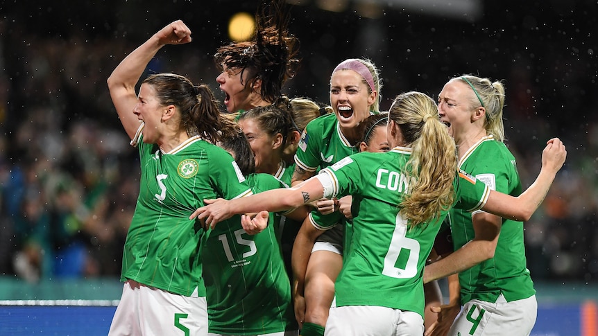 A group of excited Irish women's footballers smile, pile together and punch the air in celebration. 