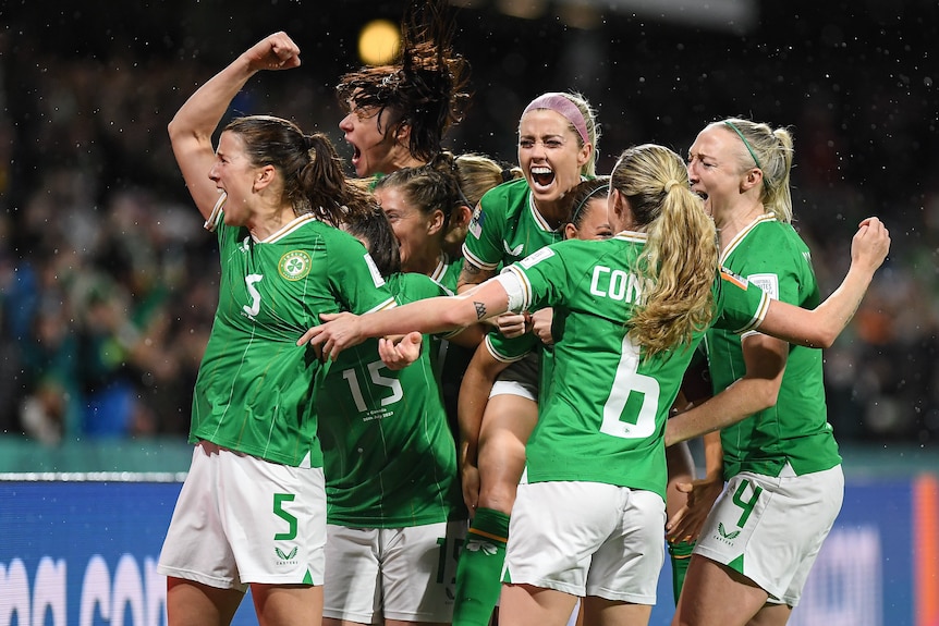 A group of excited Irish women's footballers smile, pile together and punch the air in celebration. 