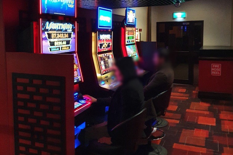 Two blurred faced people play the pokies at a pub