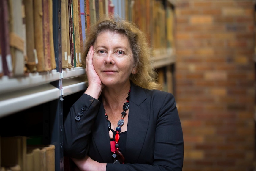 A woman leans against a bookcase inside a library.