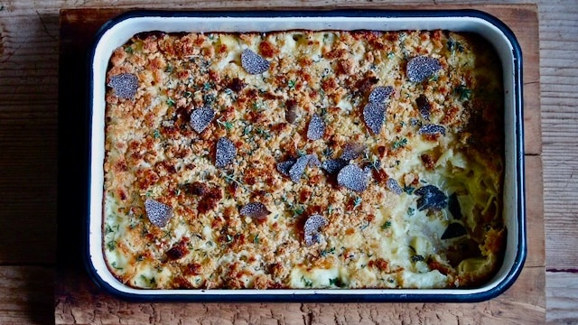 A baking pan with cooked mac and cheese in it and truffles on top, a scoop taken out of one corner