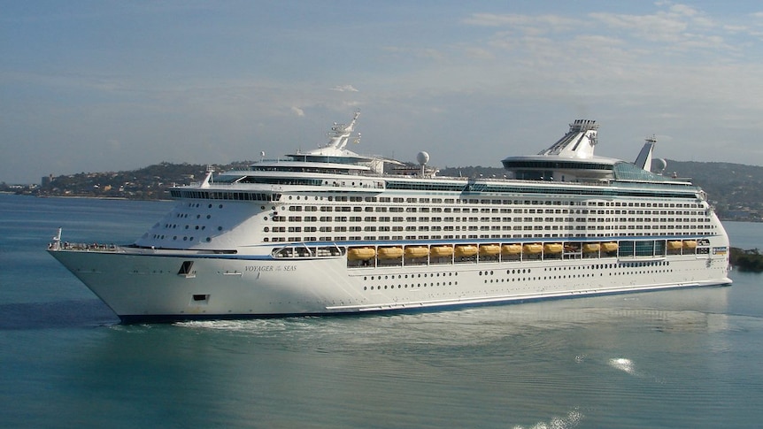 Wide shot of cruise ship Voyager of the Seas turning in a harbour with houses on a hill in the background