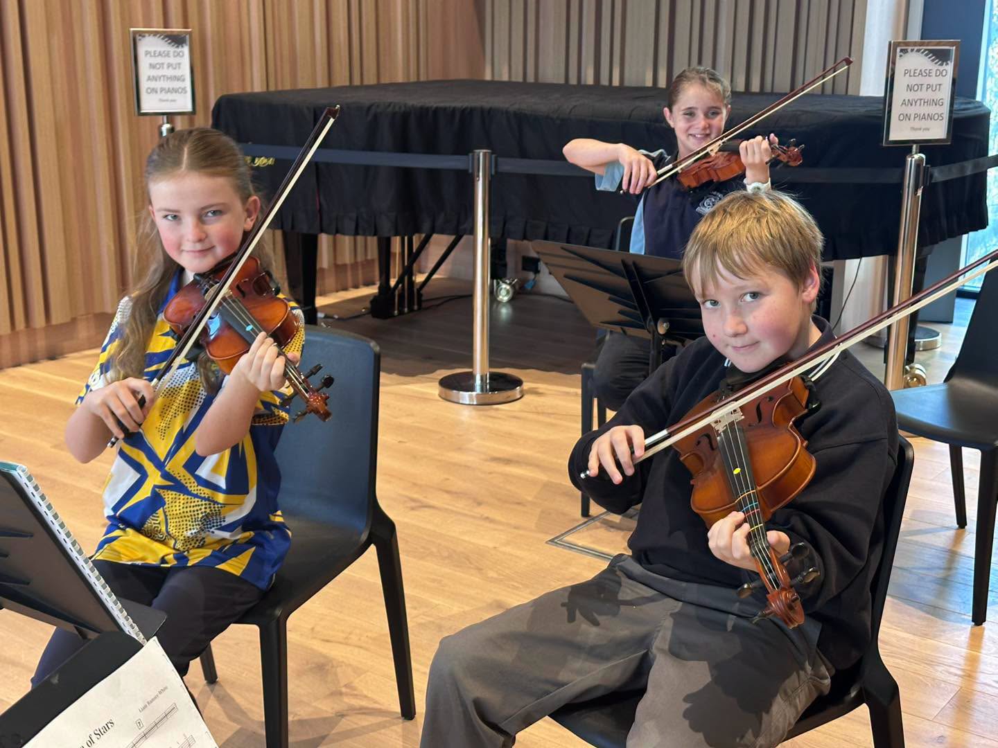 Three students hold violins below their chins and smile at the camera 
