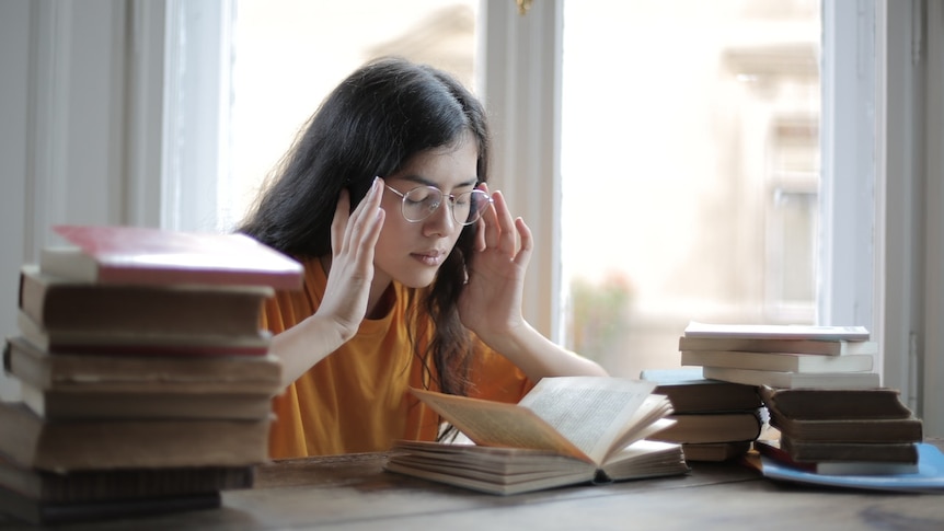 Dark haired woman holds her head in her hands 