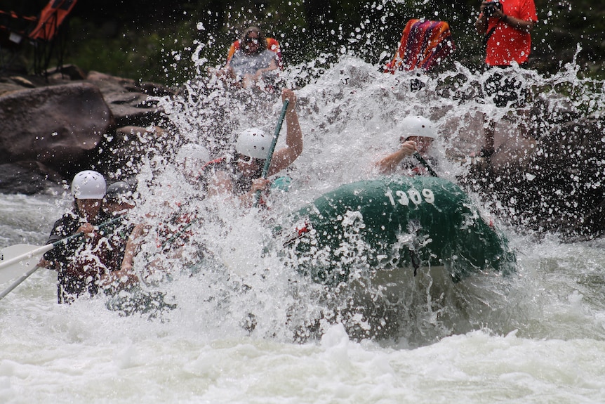 A rafting boat is covered in white water as the water splashes.