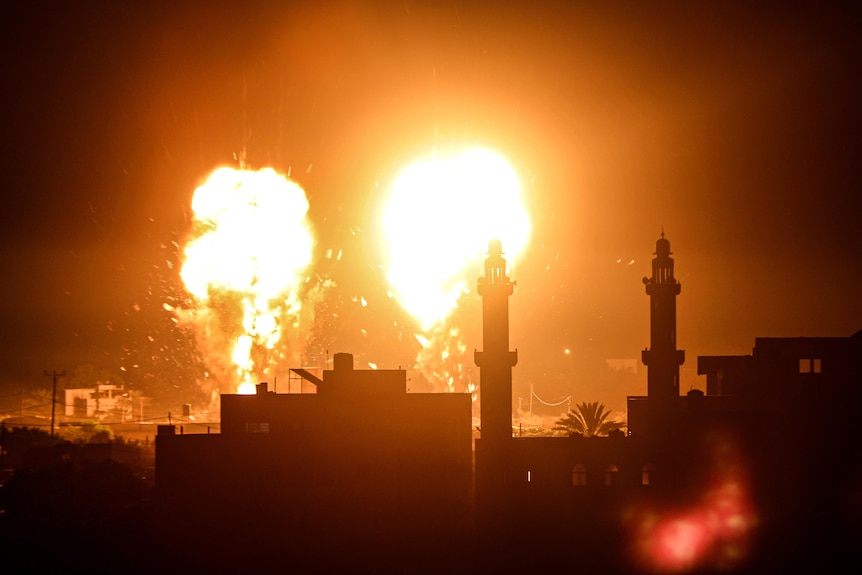 Flames shoot into the night sky behind towers in Gaza.