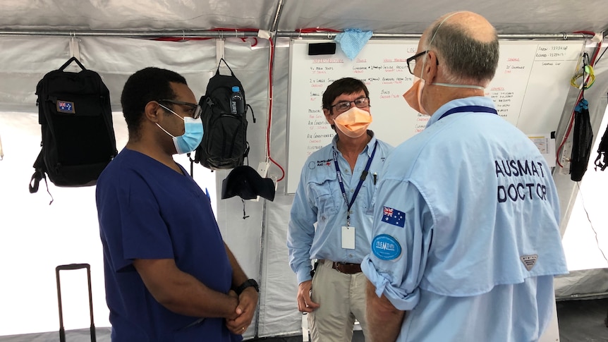 Three men wearing masks talk to each other.