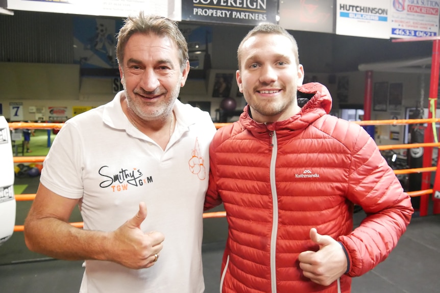 Two men smiling at the camera with their thumbs up. 