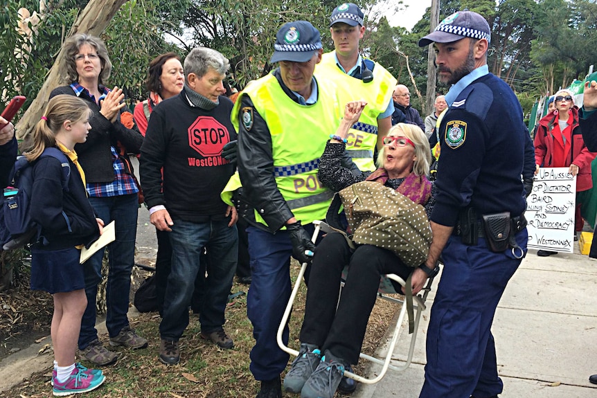 Two police officers carry a away a protester seated on a chair