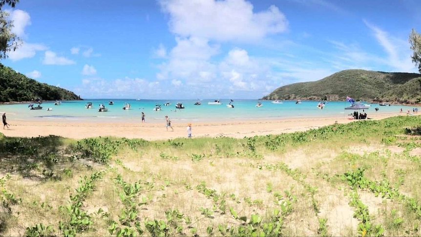 People standing along the beach of an island in North Queensland with boats in the distance.