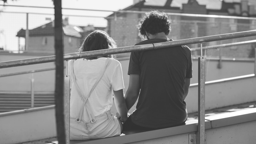 A young couple sitting holding hands.