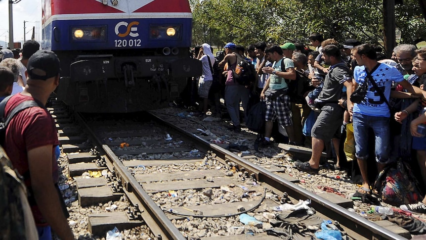 Migrants sitting along a railway track as a train approaches the Greek-Macedonian border