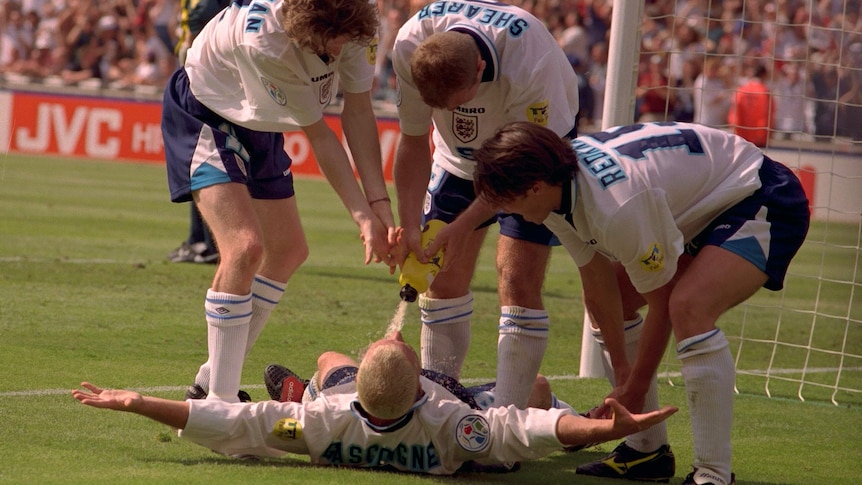 Three England footballers pour water into Paul Gascoigne's mouth.