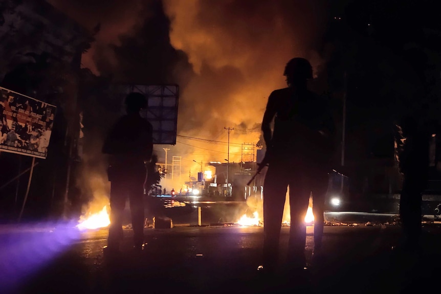 Gun-totting guards stand silhouetted in the dark as fires burn in the street behind them