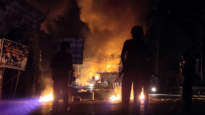 Gun-totting guards stand silhouetted in the dark as fires burn in the street behind them