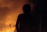 Gun-totting guards stand silhouetted in the dark as fires burn in the street behind them