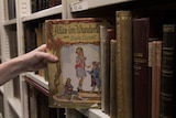 Paul Bray pulls out a worn copy of Lewis Carroll's Alice in Wonderland book from the archive shelf