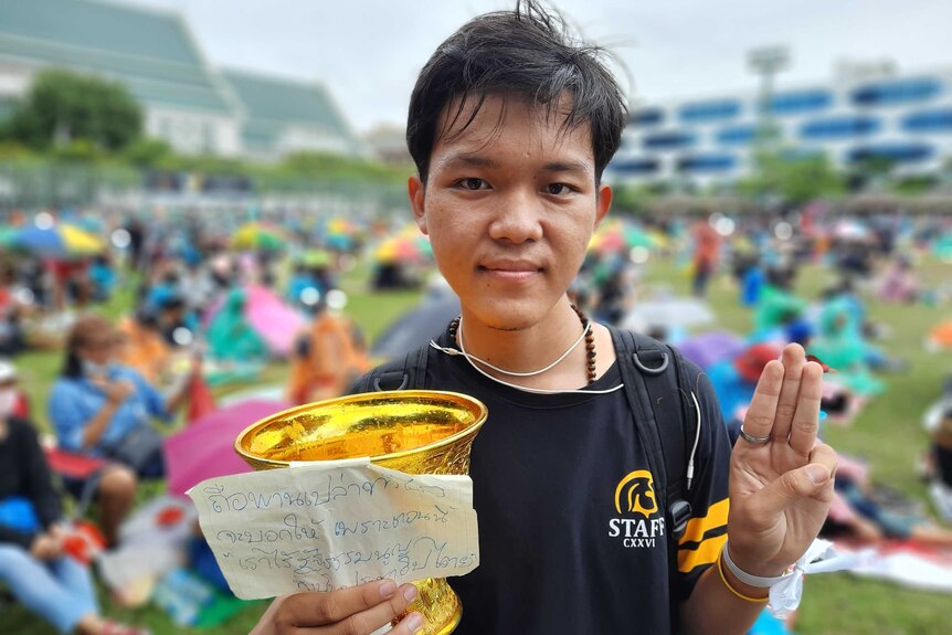 A young Thai students holds an empty gold plastic cup with a sign on it saying 'chase democracy away'.