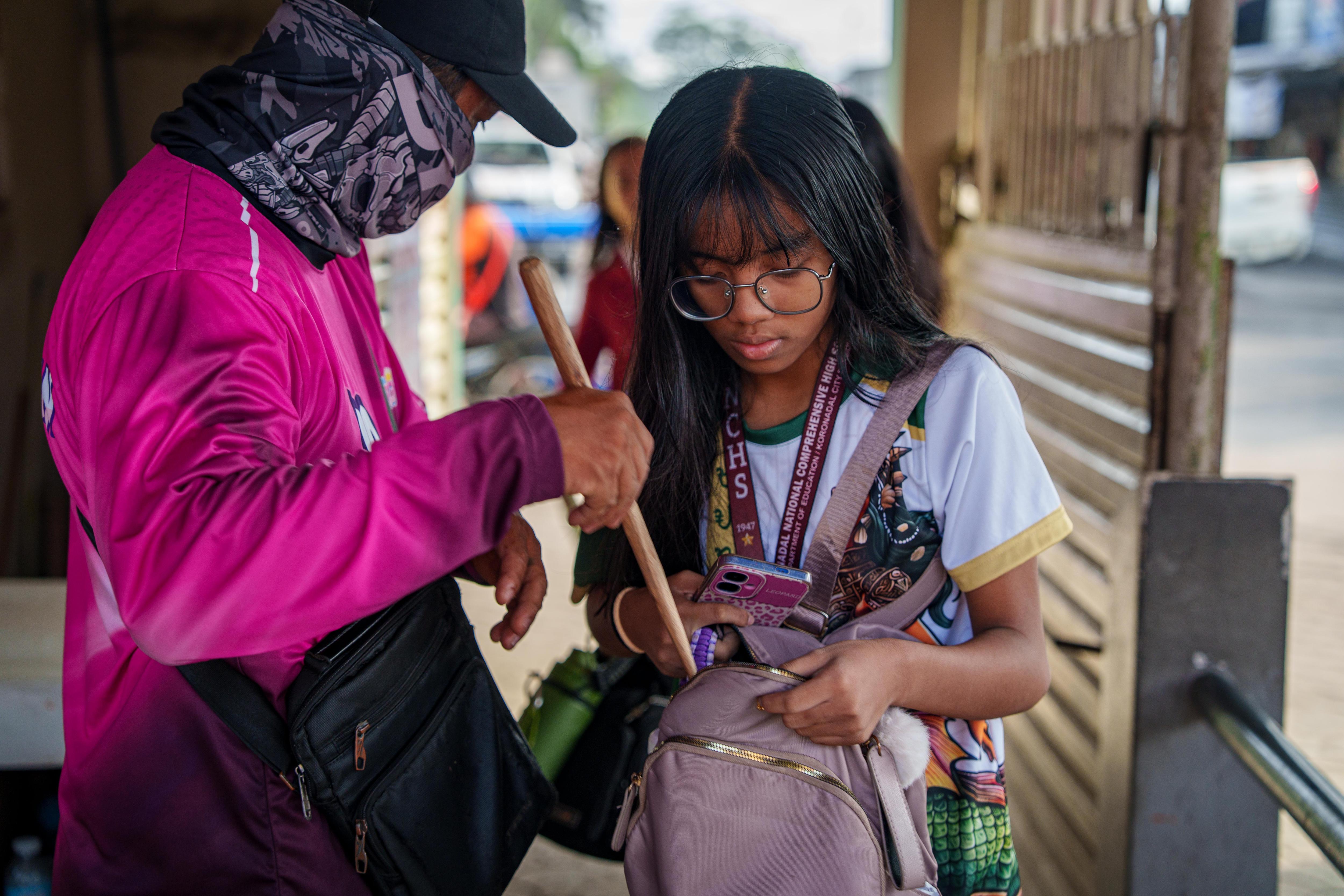 A Filipino school girl holds open her backpack while a security guard looks through its contents.