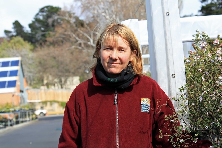 Woman wearing a red polar fleece jacket standing next to some plants in a nursery