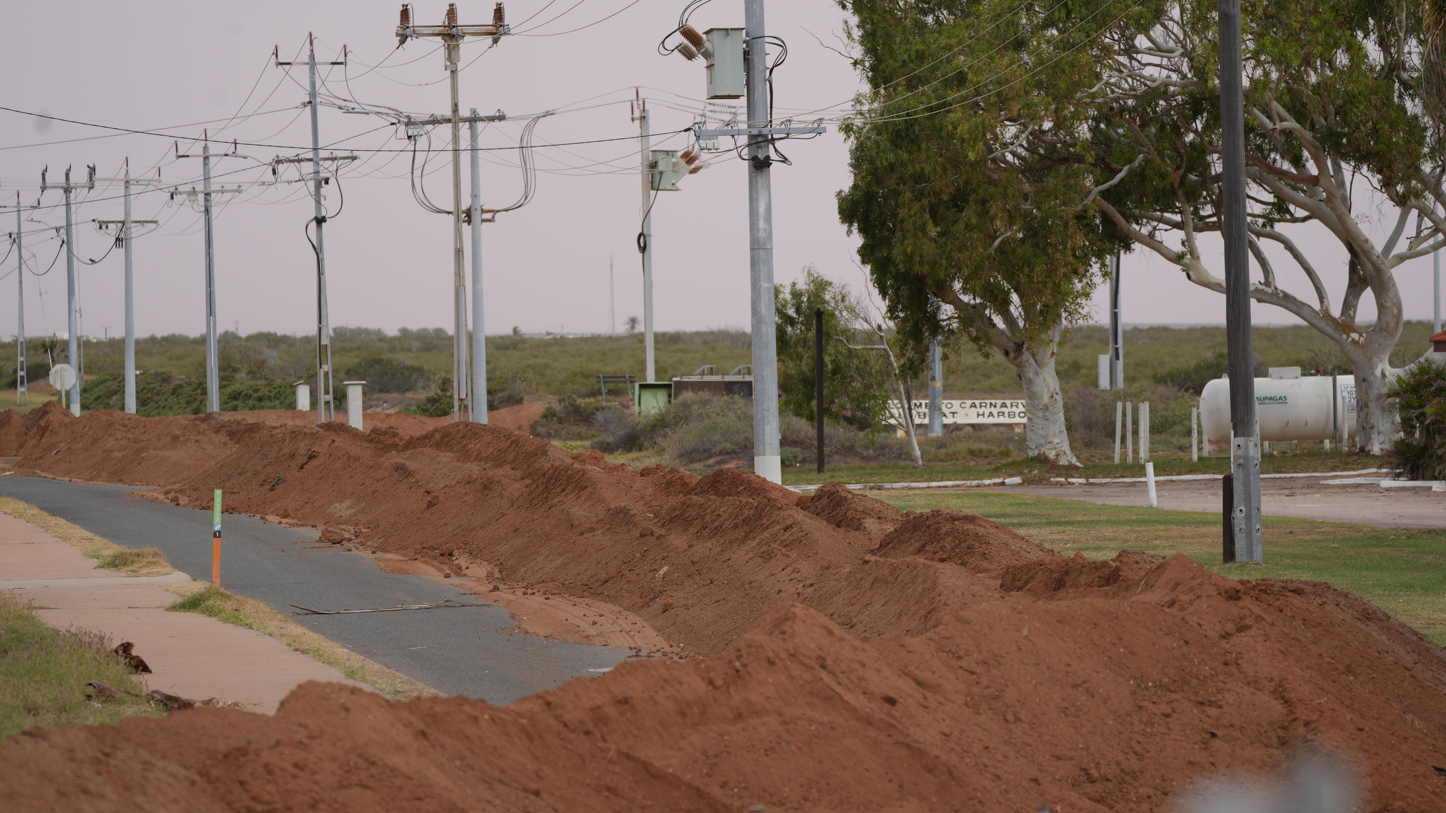 A road lined with a dirt wall and powerlines on right side
