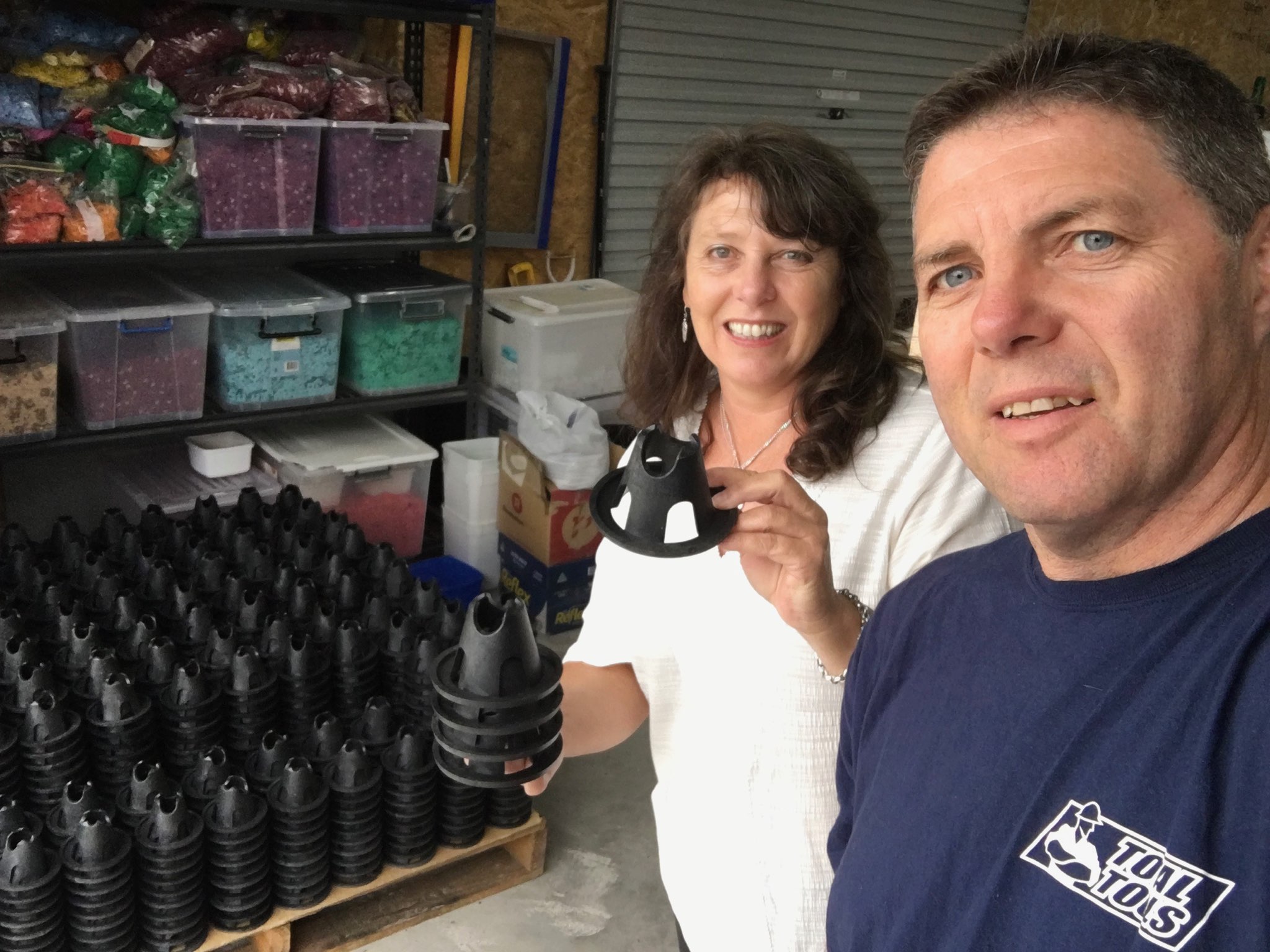 A woman and a man holding a small black plastic object with lots of them behind them