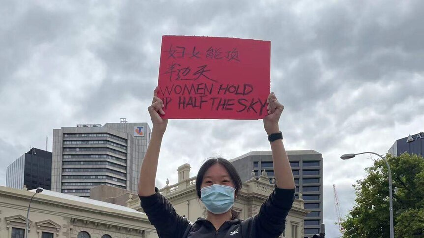 一位年轻的华裔女士举着“妇女撑起半边天”的牌子