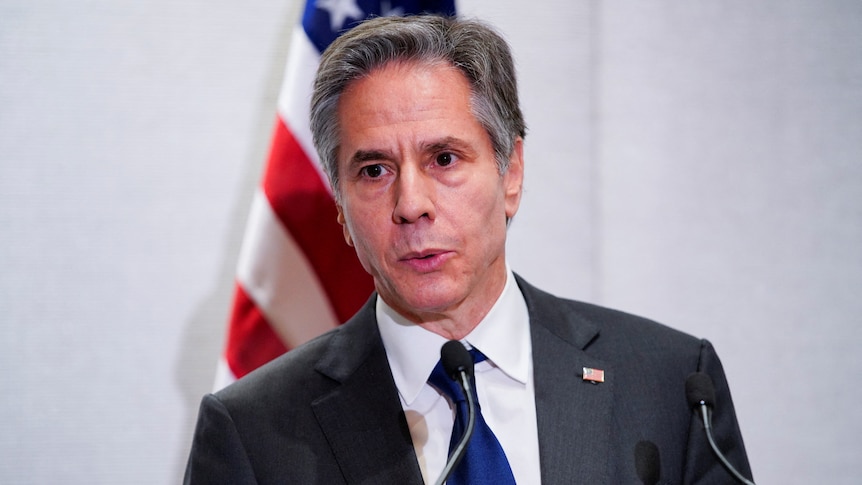 Close up of Anthony Blinken speaking at lectern with US flag behind him.