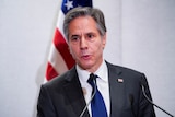 Close up of Anthony Blinken speaking at lectern with US flag behind him.