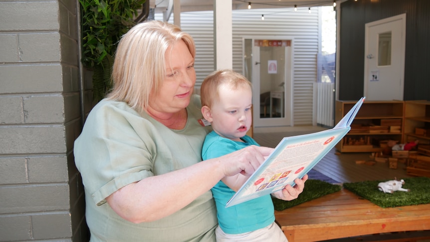 A woman wearing a green shirt is reading a book to a young boy.