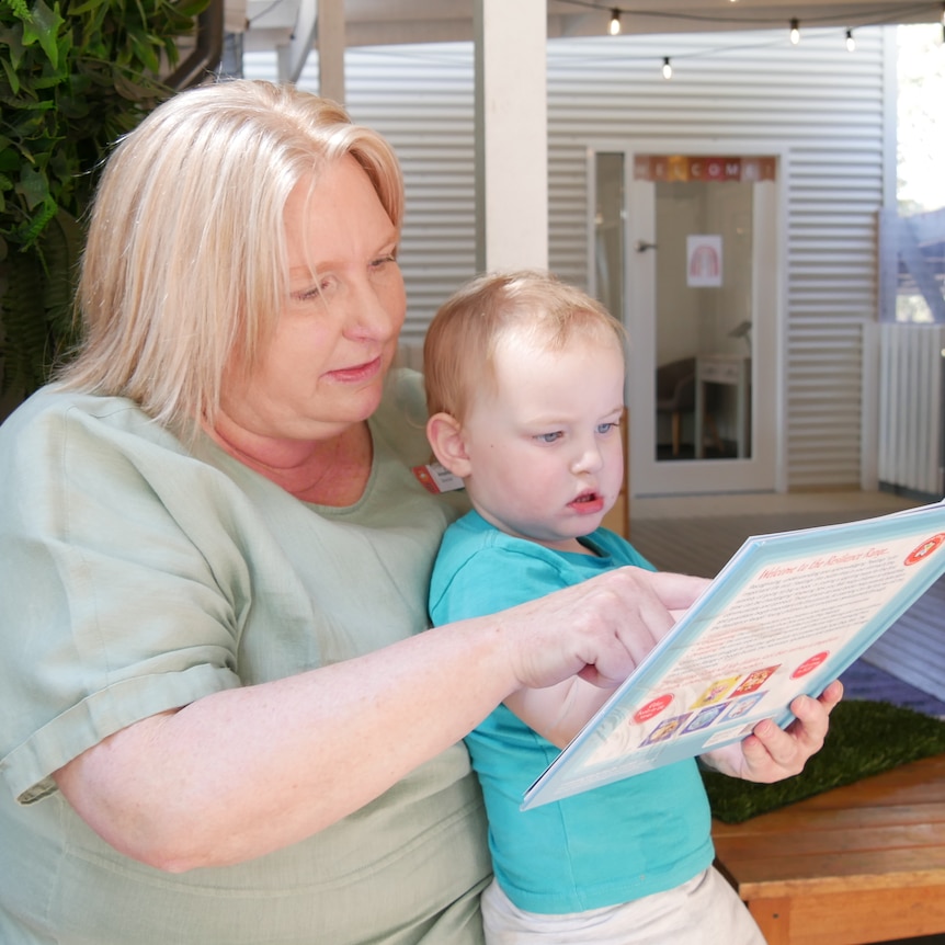 A woman wearing a green shirt is reading a book to a young boy.