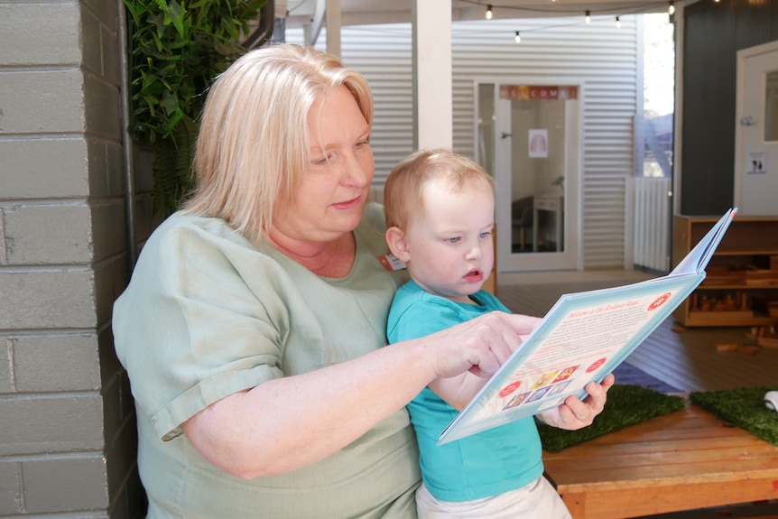 A woman wearing a green shirt is reading a book to a young boy.
